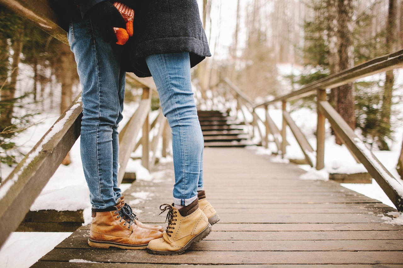 Man kissing young woman standing on toes outdoors in winter park