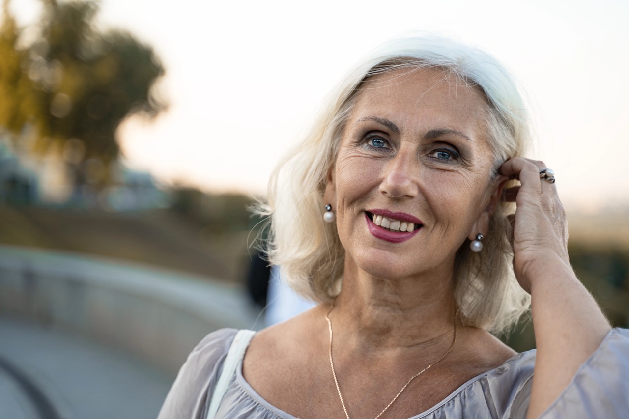 portrait of a beautiful gray-haired european woman who straightens her hair. blue eyed caucasian woman in gray dress smiling and looking into the camera